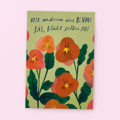Karte mit orangefarbenen Blumen und dem Spruch 'Wer anderen eine Blume sät, blüht selber auf' auf grünem Hintergrund