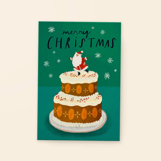 Weihnachtskarte mit zweistöckigem Kuchen, oben eine kleine Figur des Weihnachtsmanns, umgeben von Schneeflocken, Text 'merry CHRISTMAS'.
