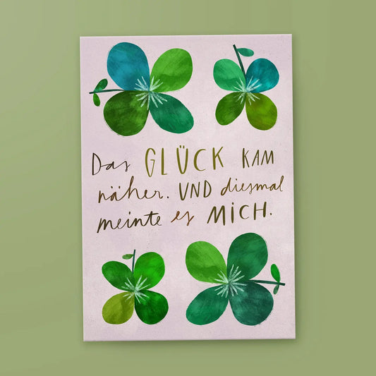 Illustration von vier vierblättrigen Kleeblättern in verschiedenen Grüntönen auf einem zartrosa Hintergrund. Mittig steht der Text: „Das GLÜCK KAM näher. UND diesmal meinte es MICH.“