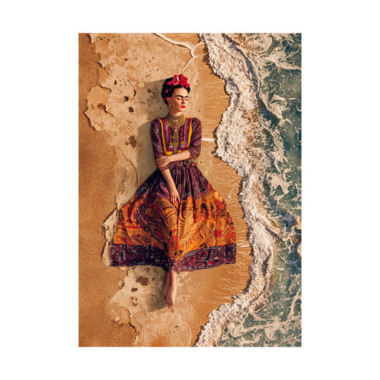 Vogelperspektive einer Frau im Frida-Kahlo-Look mit geschlossenem Blick, die barfuß in einem aufwendig gemusterten Kleid am Sandstrand liegt, während sanfte weiße Meereswellen sie umspülen.