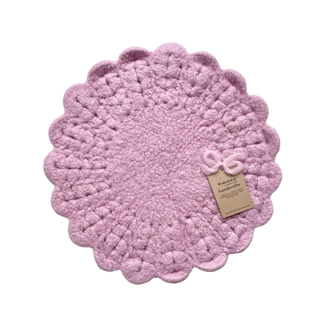 Eine handgehäkelte Sitzunterlage in Rosa mit romantischen Blütensaum. Das zentrale Häkelmuster in Kreisform bildet einen harmonischen Kontrast zum verspielten Rand. 