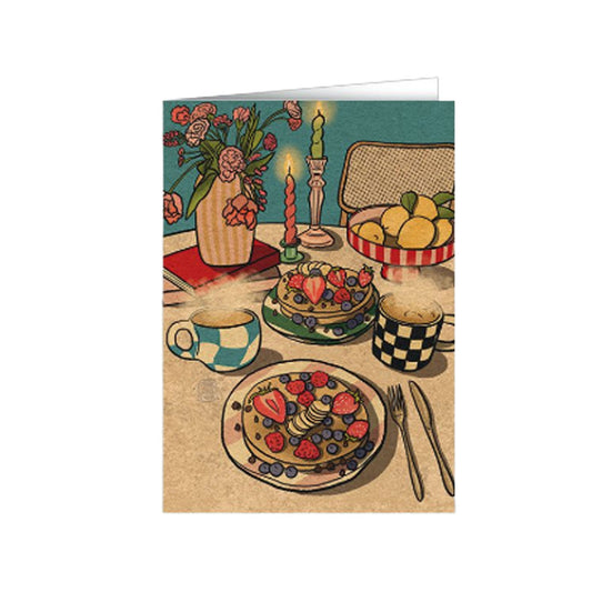 Illustration eines gemütlichen Frühstückstisches mit Blaubeer-Erdbeer-Pancakes, zwei Tassen Kaffee, Blumen und Zitronen.