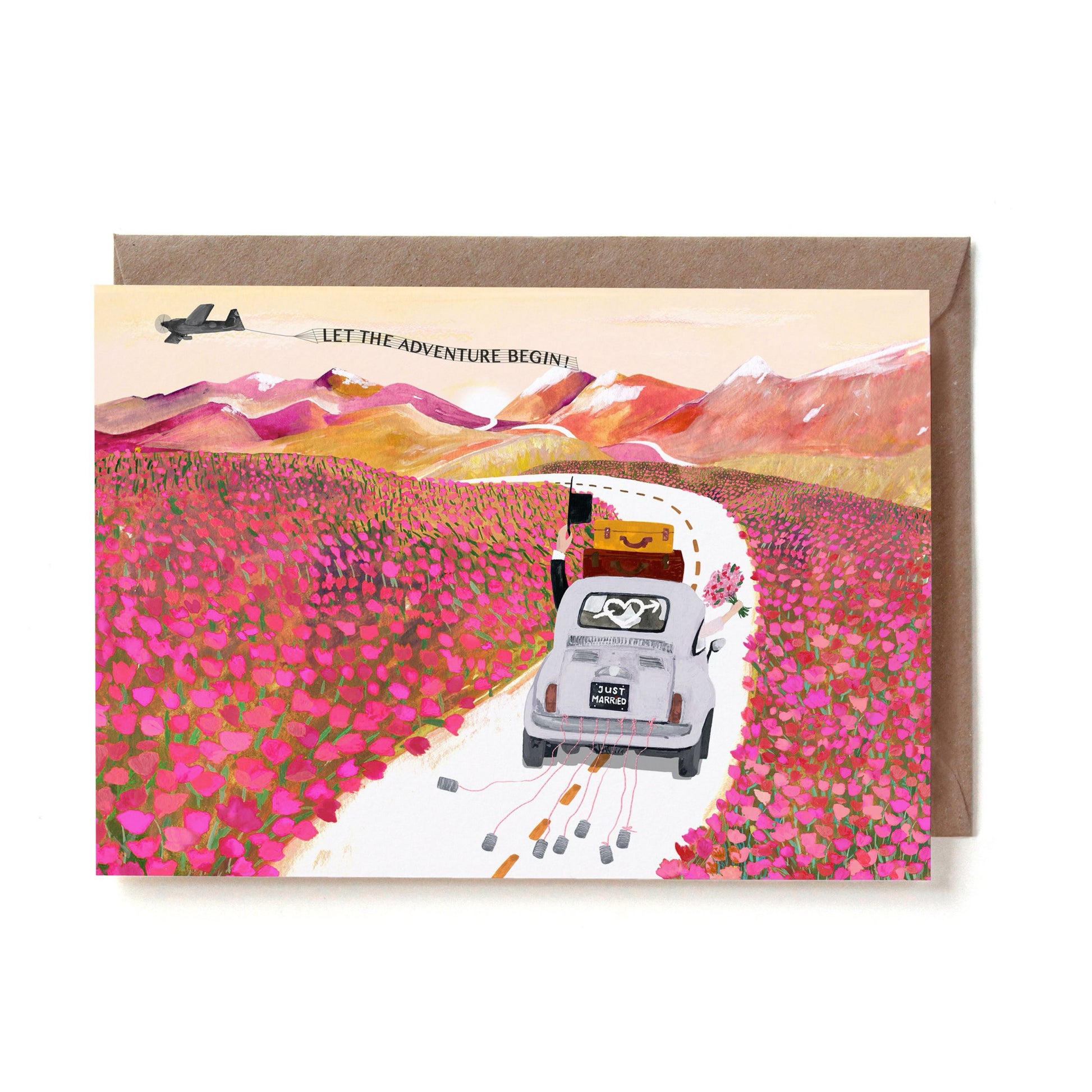 Eine illustrierte Hochzeitskarte im Querformat. Ein weißer Oldtimer-Käfer mit zwei Koffern auf dem Dach und einem „JUST MARRIED“-Nummernschild fährt eine geschwungene Straße entlang, während Blechdosen an Schnüren hinterhergezogen werden. Das Auto fährt durch ein riesiges, leuchtend pinkes Feld voller Blumen auf herbstliche, rötliche Berge zu. Am Himmel fliegt ein kleines Flugzeug, das ein Banner mit der Aufschrift „LET THE ADVENTURE BEGIN!“ hinter sich herzieht. Die Karte liegt auf einem braunen Kraftpapie
