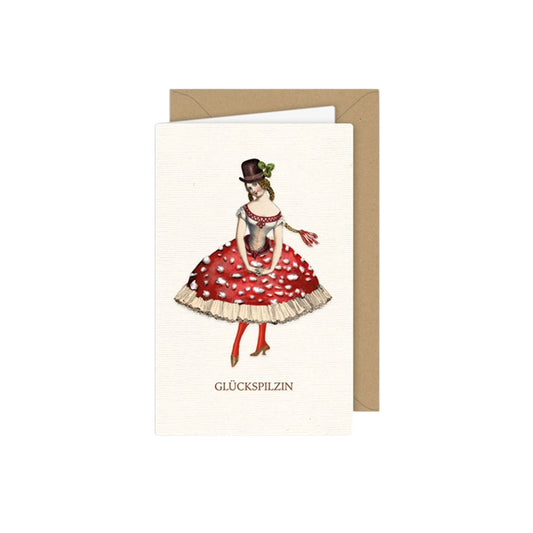 Vintage-Grußkarte mit einer Frau im Kleid, dessen Rock wie ein Fliegenpilz gestaltet ist. Sie trägt einen braunen Zylinder mit Kleeblatt und eine geflochtene Frisur. Unten steht der Text „GLÜCKSPILZIN“.
