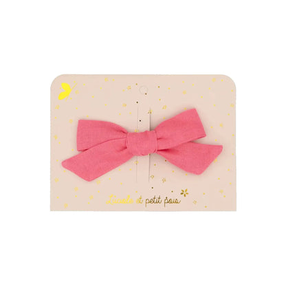 Eine handgefertigte Haarschleife aus himbeerrosa Leinenstoff, befestigt auf einer hellrosa Präsentationskarte mit goldenem 'Luciole et petit pois' Schriftzug und Sternen