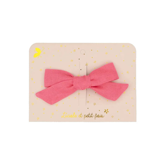 Eine handgefertigte Haarschleife aus himbeerrosa Leinenstoff, befestigt auf einer hellrosa Präsentationskarte mit goldenem 'Luciole et petit pois' Schriftzug und Sternen
