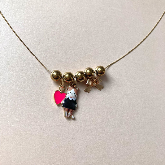 Goldene Kette mit drei Anhängern: ein pinkes Herz, eine süß illustrierte Katze und eine kleine goldene Schleife.