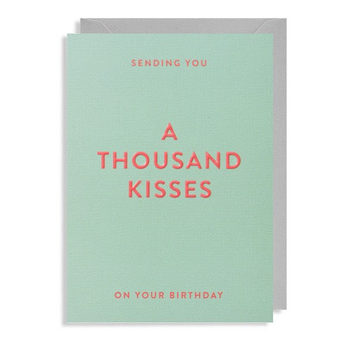 Mintgrüne Geburtstagskarte mit korallfarbener Prägeschrift „A THOUSAND KISSES ON YOUR BIRTHDAY“ und grauem Briefumschlag.