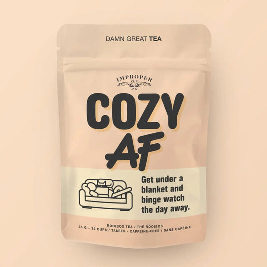 Beigefarbene Verpackung des koffeinfreien Rooibos-Tees „Cozy AF“ von Improper Cup mit einer Strichzeichnung von einem Sofa.
