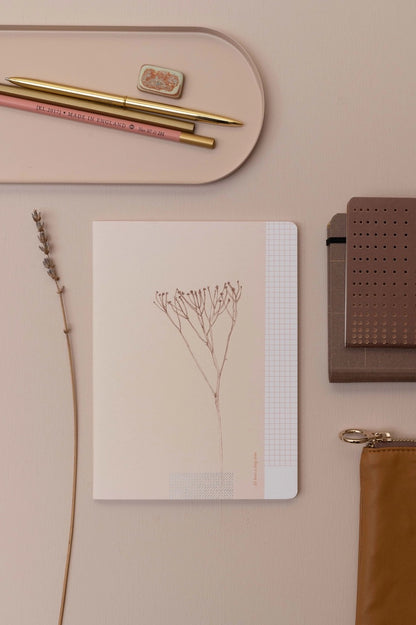 Draufsicht auf das botanische Notizheft, umgeben von farblich abgestimmten Schreibaccessoires wie goldenen Stiften, einer Lavendelblüte und einem Etui in Erdtönen.