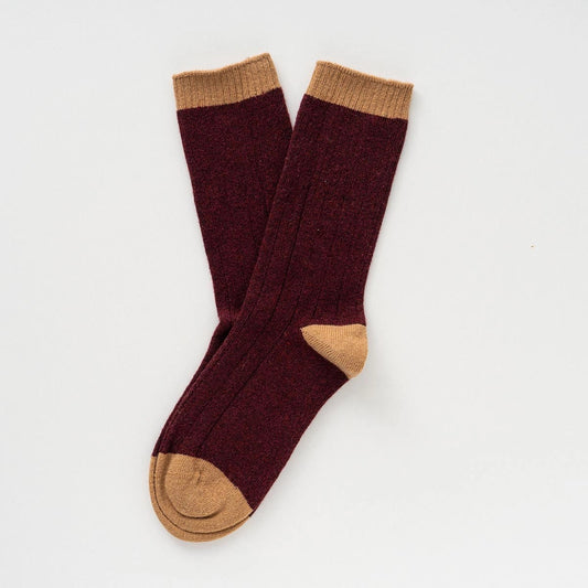 Ein Paar dunkelrote KLUE Merinowolle-Socken mit hellbraunem Bund, Ferse und Spitze im Rippstrick-Design.