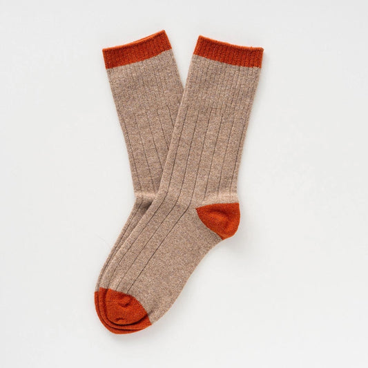 Ein Paar beigefarbene KLUE Merinowolle-Socken mit orangefarbenem Bund, Ferse und Spitze im Rippstrick-Design.