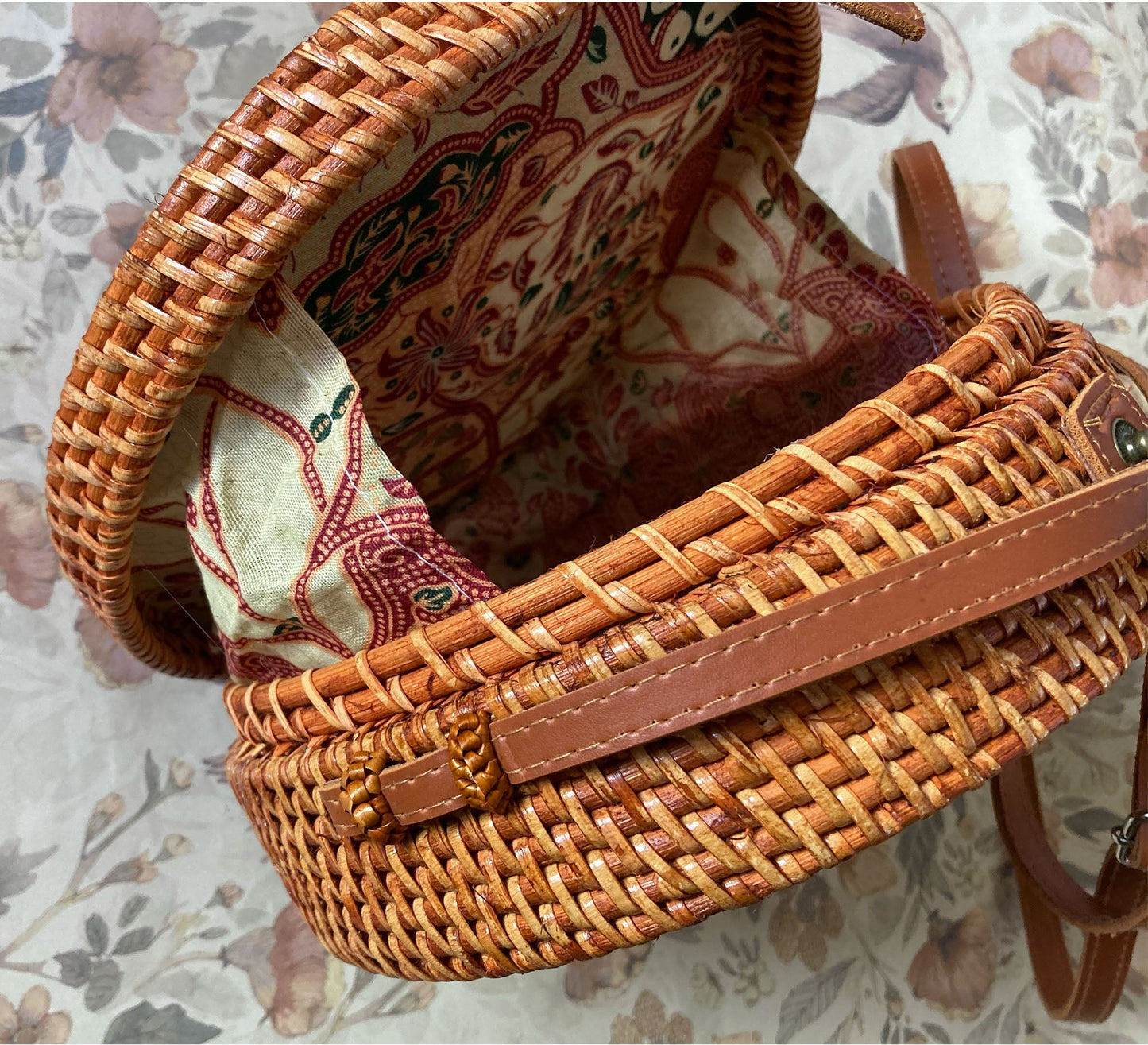 Innenansicht einer runden Rattan-Tasche mit farbenfrohem Batik-Innenfutter in Rot- und Beigetönen und einem Metalldruckknopf-Verschluss.
