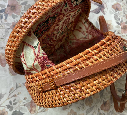 Innenansicht einer runden Rattan-Tasche mit farbenfrohem Batik-Innenfutter in Rot- und Beigetönen und einem Metalldruckknopf-Verschluss.