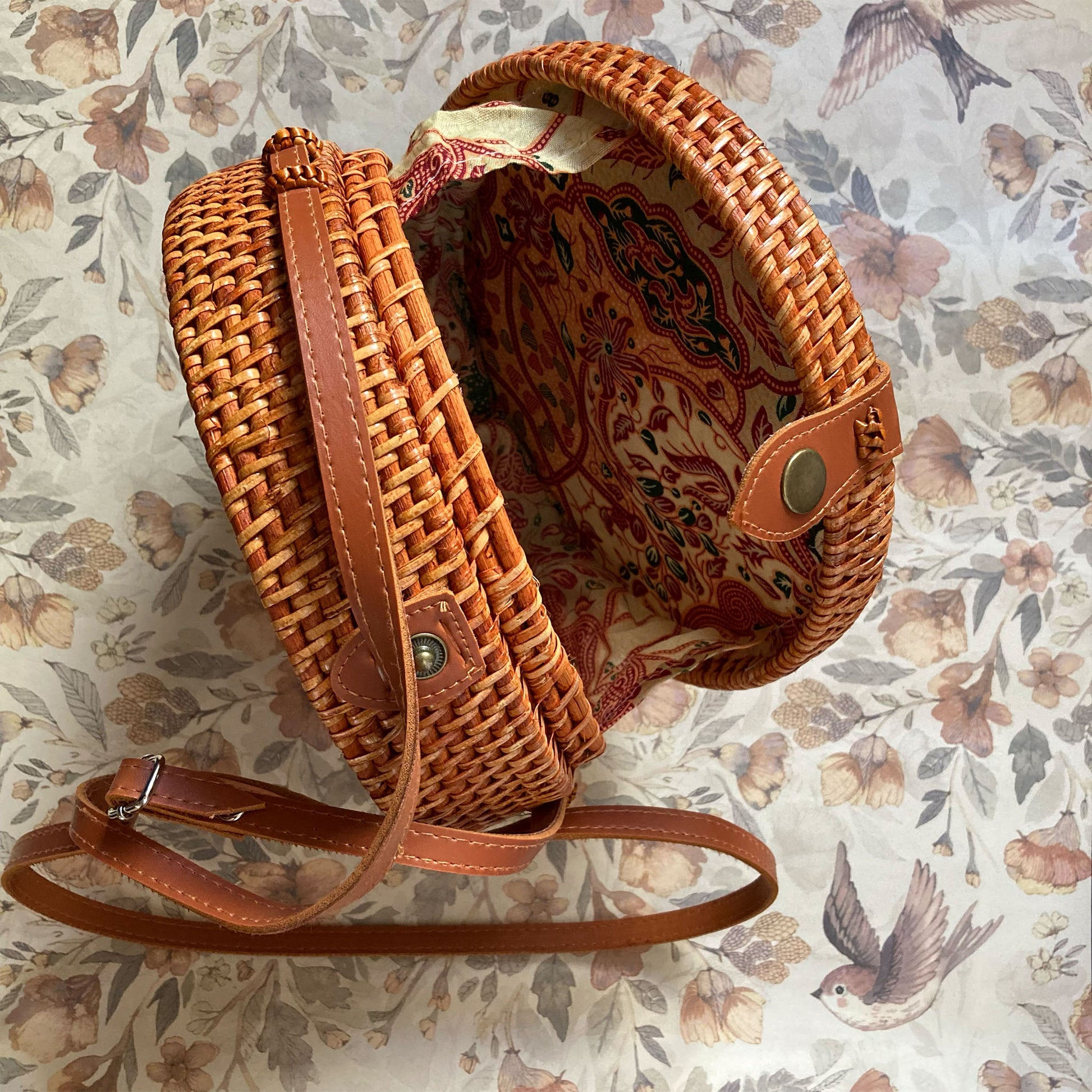 Innenansicht einer runden Rattan-Tasche mit farbenfrohem Batik-Innenfutter in Rot- und Beigetönen und einem Metalldruckknopf-Verschluss.