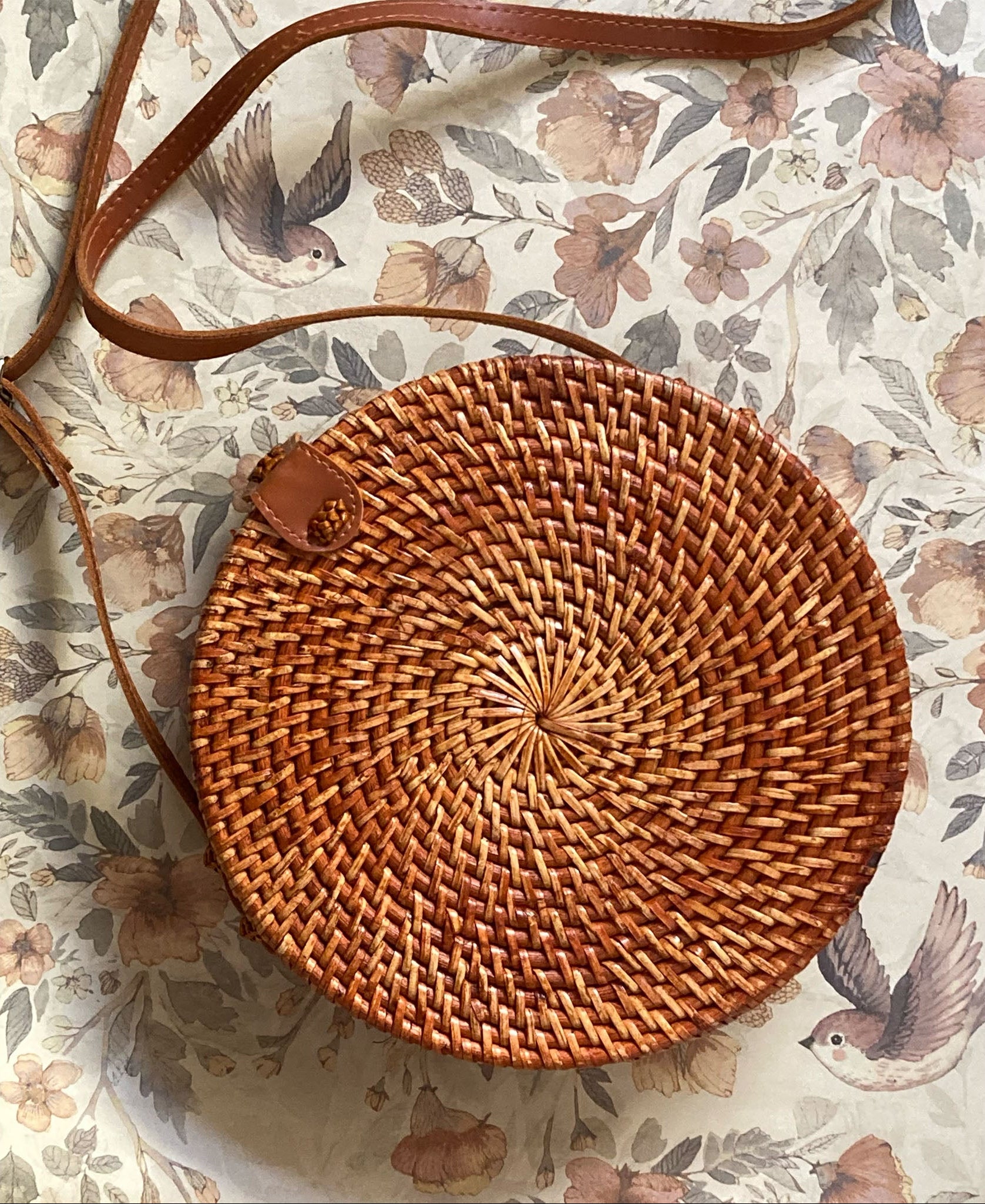 Detailaufnahme des kreisförmigen Flechtmusters einer braunen Rattan-Tasche auf einem floralen Hintergrund.