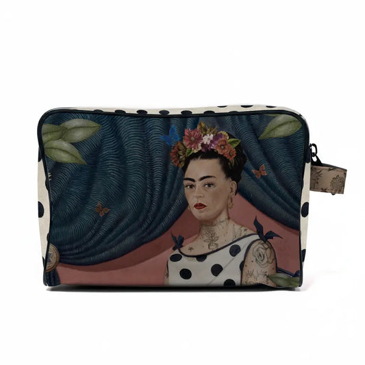 Vorderseite der voglio bene Kulturtasche mit einem kunstvollen Porträt von Frida Kahlo. Sie trägt einen bunten Blumenkranz im Haar, ein gepunktetes Kleid und feine Tattoos an Hals und Schultern. Der Hintergrund zeigt einen dunkelblauen, drapierten Vorhang mit Schmetterlingen.