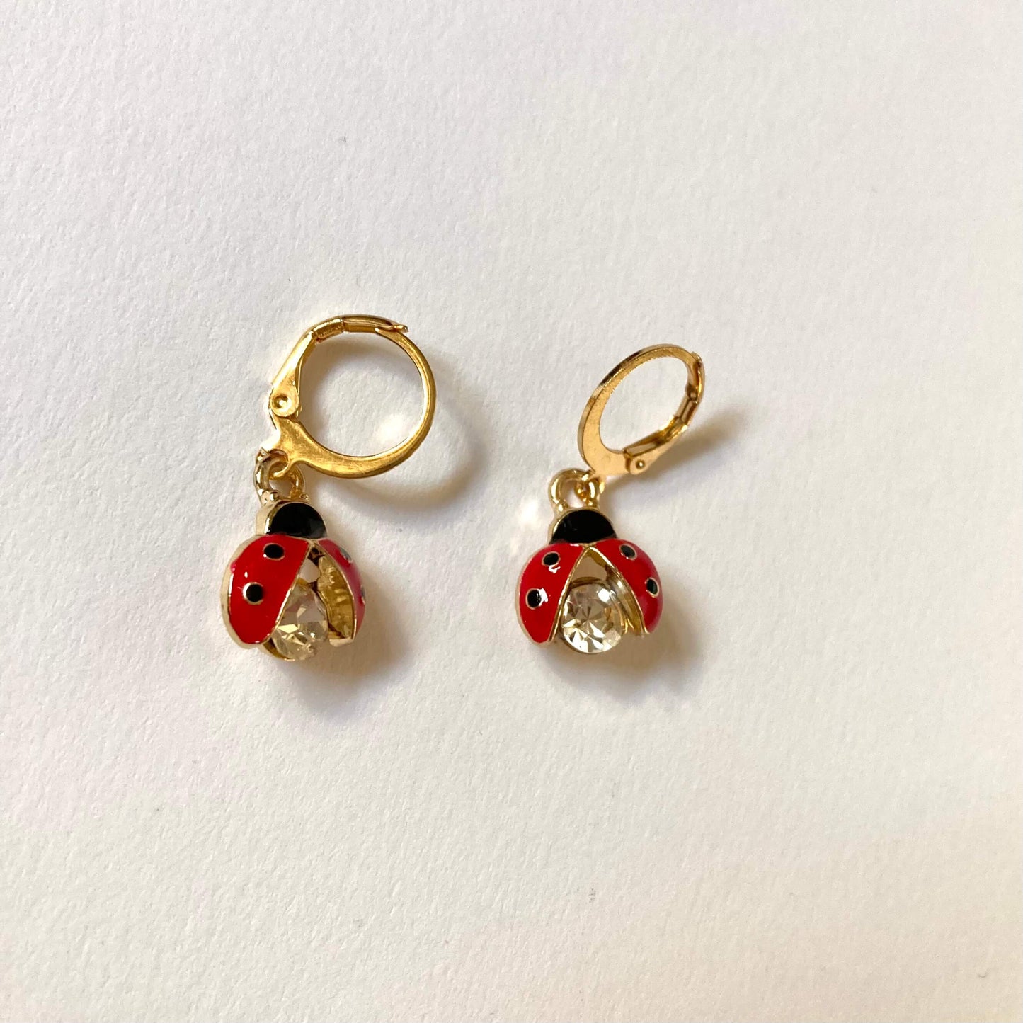 Goldene Creolen-Ohrringe mit Marienkäfer-Anhängern. Die Marienkäfer haben rote Flügel mit schwarzen Punkten und einen großen, funkelnden Kristall-Körper.