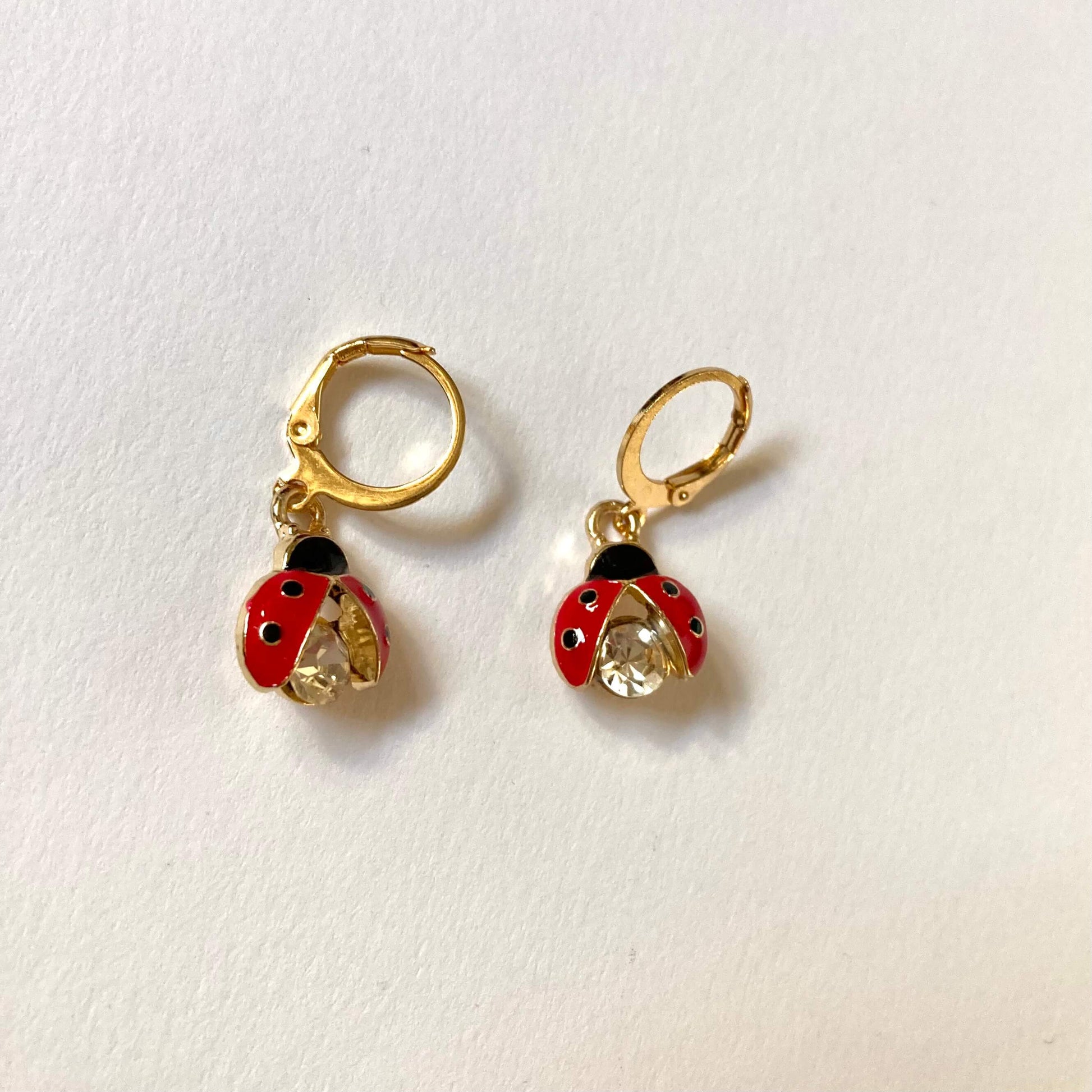 Goldene Creolen-Ohrringe mit Marienkäfer-Anhängern. Die Marienkäfer haben rote Flügel mit schwarzen Punkten und einen großen, funkelnden Kristall-Körper.