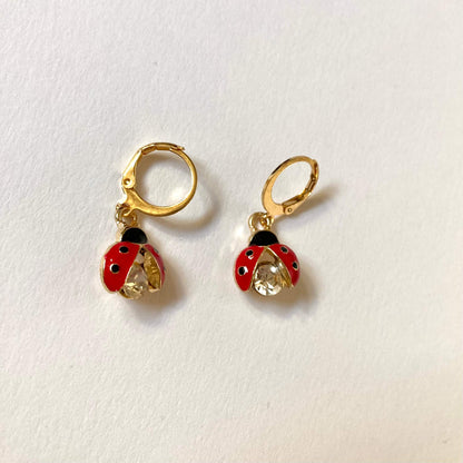 Goldene Creolen-Ohrringe mit Marienkäfer-Anhängern. Die Marienkäfer haben rote Flügel mit schwarzen Punkten und einen großen, funkelnden Kristall-Körper.