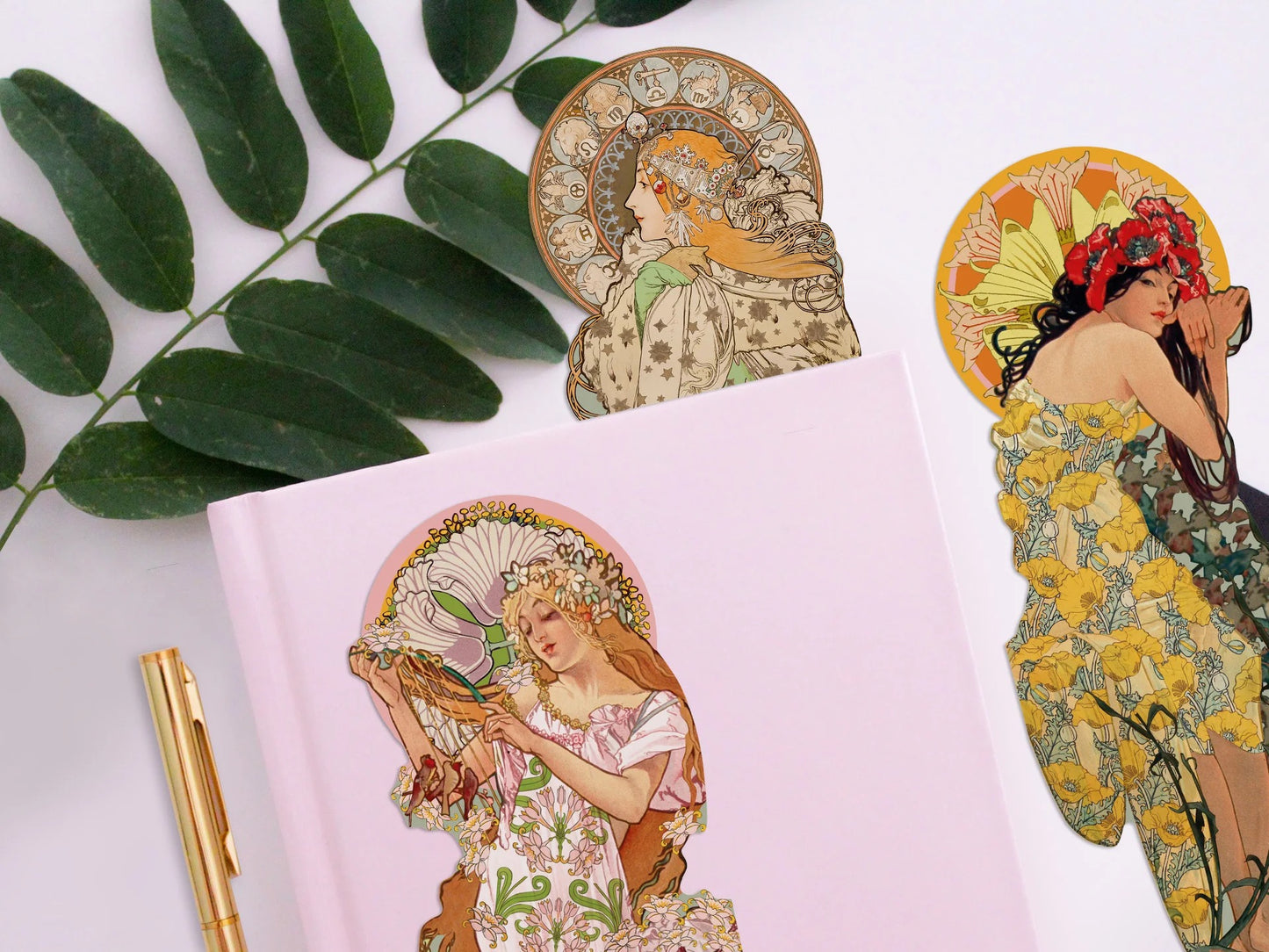 Ein zartrosa Notizbuch auf hellem Hintergrund, flankiert von einem grünen Zweig und einem goldenen Stift. Ein Lesezeichen einer seitlich blickenden Renaissance-Frau im dunkel gemusterten Kleid mit weißen Rosen in den Händen liegt auf dem Buch, während im Hintergrund zwei weitere Botticelli-Figuren zu sehen sind.