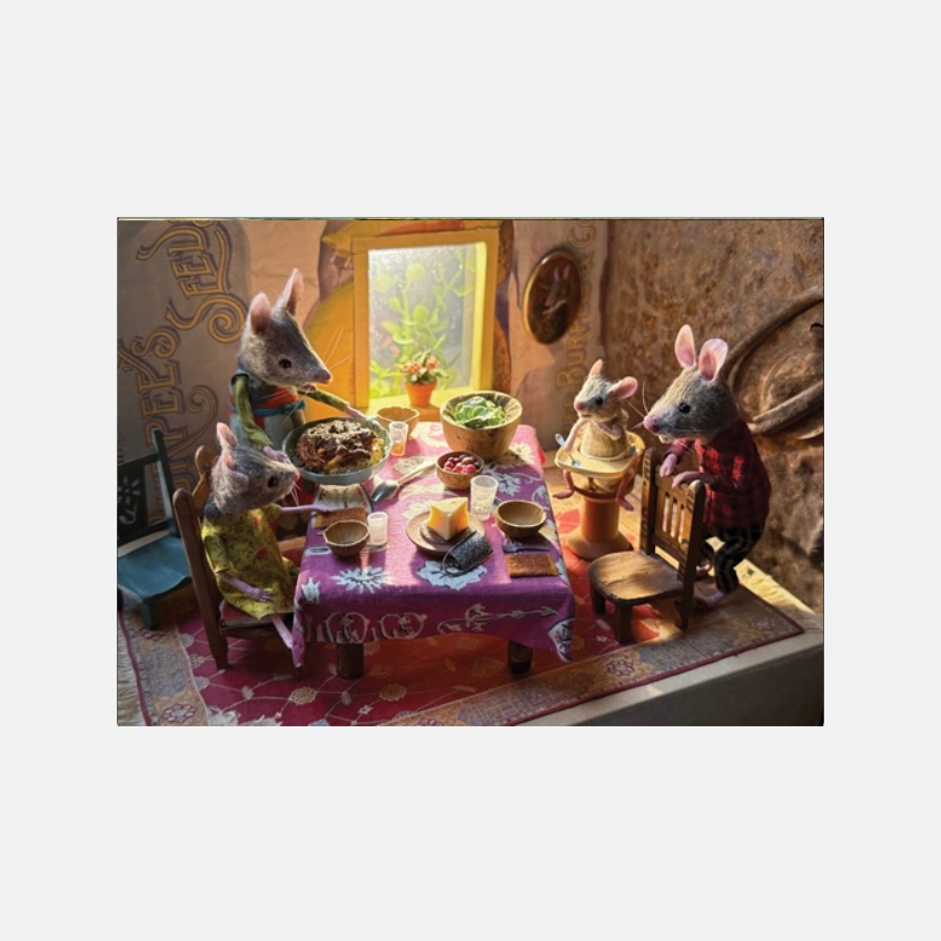 Eine detaillierte Miniatur-Szene einer Mäusefamilie beim gemeinsamen Essen. Fünf vermenschlichte Mäusefiguren in Kleidung sitzen an einem kleinen Tisch mit rosa Tischdecke, auf dem verschiedene Speisen und ein Stück Käse serviert sind. Ein Mäusekind sitzt in einem Hochstuhl, während im Hintergrund ein kleines Fenster warmes Licht hereinlässt.