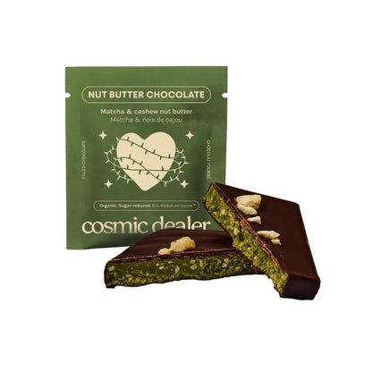 Grüne Verpackung der Cosmic Dealer Schokolade neben zwei Riegelstücken, die die leuchtend grüne Matcha-Cashew-Füllung zeigen.
