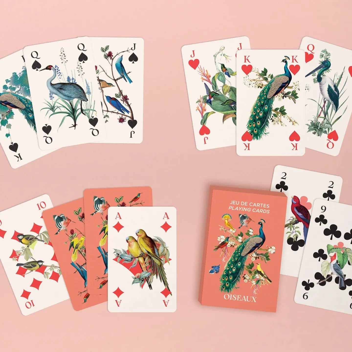 Eine Vielfalt an Spielkarten des Vögel-Decks ist zusammen mit der Produktbox dekorativ auf einer rosa Oberfläche verteilt. Oben sind Bildkarten (Könige, Damen, Buben) von Pik und Herz aufgereiht, die unterschiedliche Vögel und Pflanzen zeigen. Unten links liegen Zahlenkarten (wie die Karo 10 mit Meisen) sowie das Karo-As mit zwei bunten Papageien. Unten rechts ist die lachsfarbene Box neben zwei Kreuz-Zahlenkarten platziert.