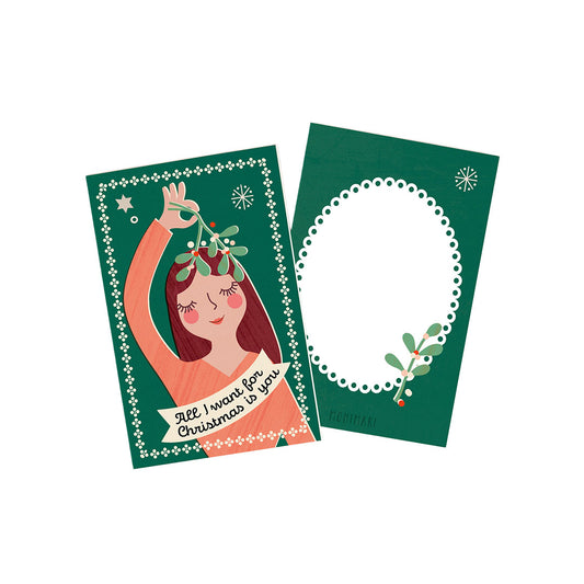Minikarte von Monimari zu Weihnachten auf grünem Hintergrund. Vorderseite: Eine Frau hält einen Mistelzweig über ihren Kopf mit Banner-Aufschrift „All I want for Christmas is you“. Rückseite: Dunkelgrüne Karte mit weißem, geperltem Oval-Rahmen und einem kleinen Mistelzweig-Akzent.