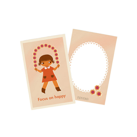Minikarte von Monimari in sanften Beige- und Rosatönen. Vorderseite: Ein Mädchen im orangefarbenen Kleid, das ein blumenverziertes Springseil hält; darunter der Schriftzug „Focus on happy“. Rückseite: Beigefarbene Karte mit weißem, geperltem Oval-Rahmen und drei kleinen Blumenmotiven unten rechts.