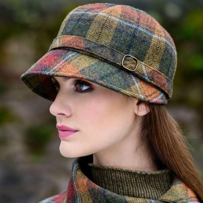 Eine Frau mit braun orangefarbenem, kariertem Flapper Hut, weißem Oberteil und schwarzem Blazer vor grünem Laub im Hintergrund.