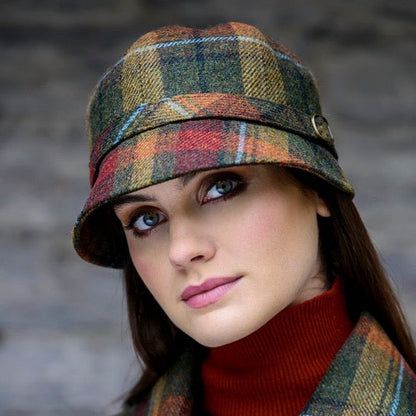 Eine Frau mit braun orangefarbenem, kariertem Flapper Hut, weißem Oberteil und schwarzem Blazer vor grünem Laub im Hintergrund.