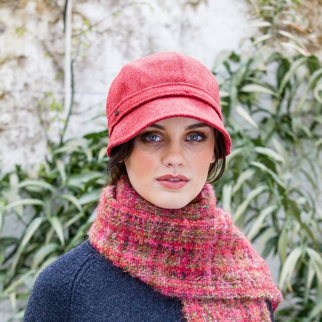 Eine Frau mit roten Flapper Hut, rot pinken Schal und dunkelblauem Oberteil vor grünem Laub im Hintergrund.