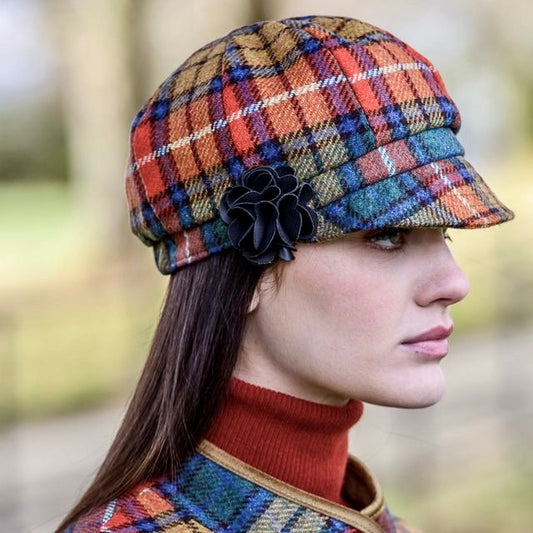 Frau mit langen braunen Haaren trägt eine rot-blau orange Karomütze und einen passenden Karomantel über einem roten Rollkragenpullover.