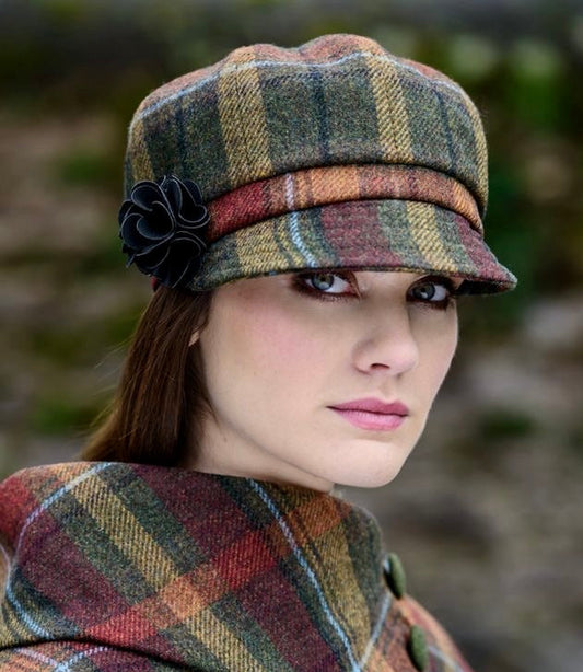 Frau  trägt karierten Mantel und passende Schirmmütze in Grün-, Rot- und Beigetönen mit schwarzer Blume als Accessoire am Hut.
