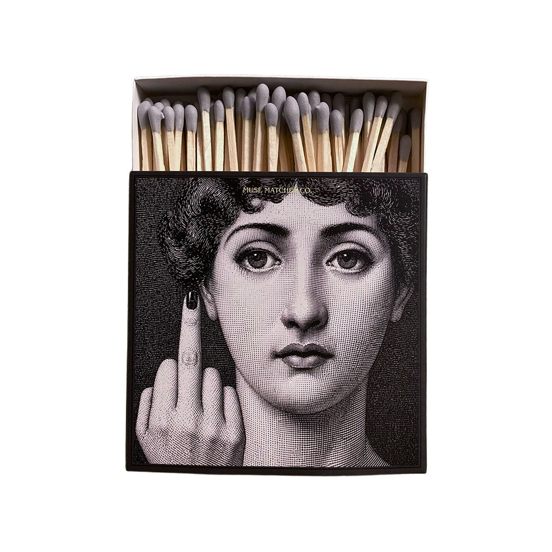 Vorderseite einer schwarzen Muse Matches Co. Streichholzschachtel mit dem Schwarz-Weiß-Porträt einer Frau, die den Mittelfinger zeigt, und grauen Streichhölzern.