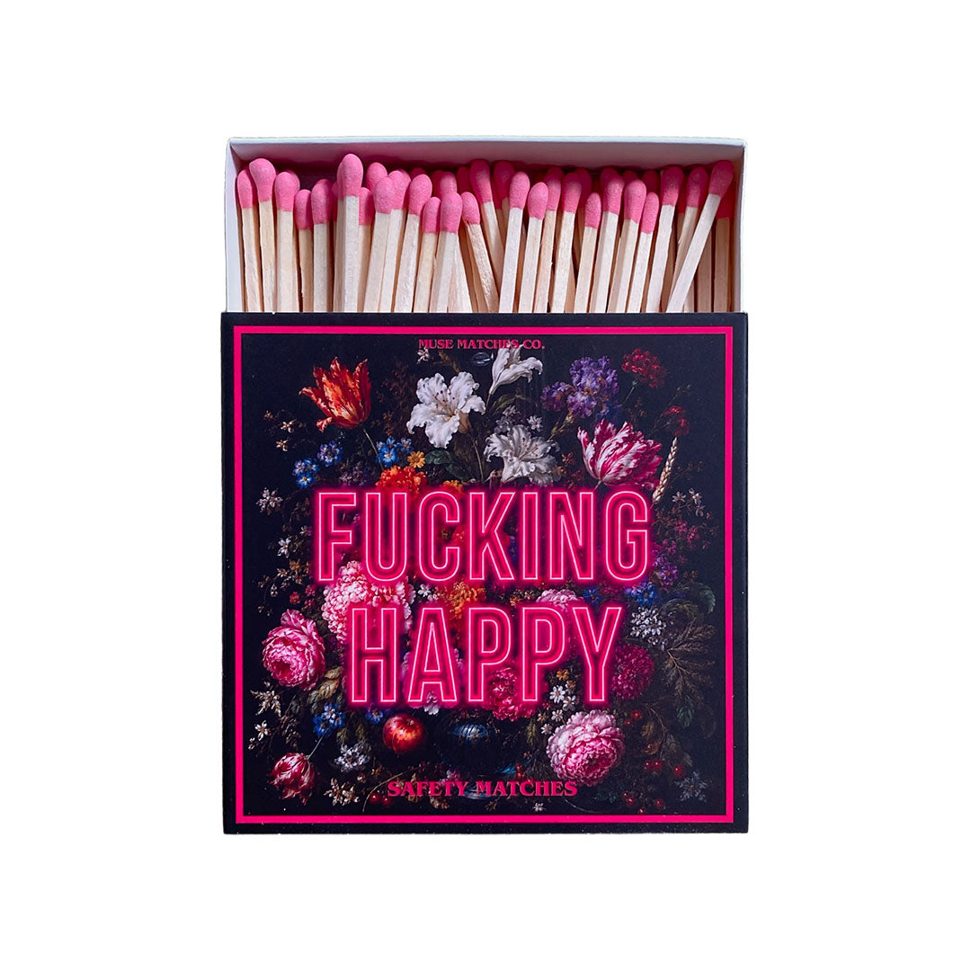 Vorderseite einer Muse Matches Co. Streichholzschachtel mit dunklem Blumen-Stillleben, leuchtend pinkem Fucking Happy Schriftzug und pinken Streichhölzern.