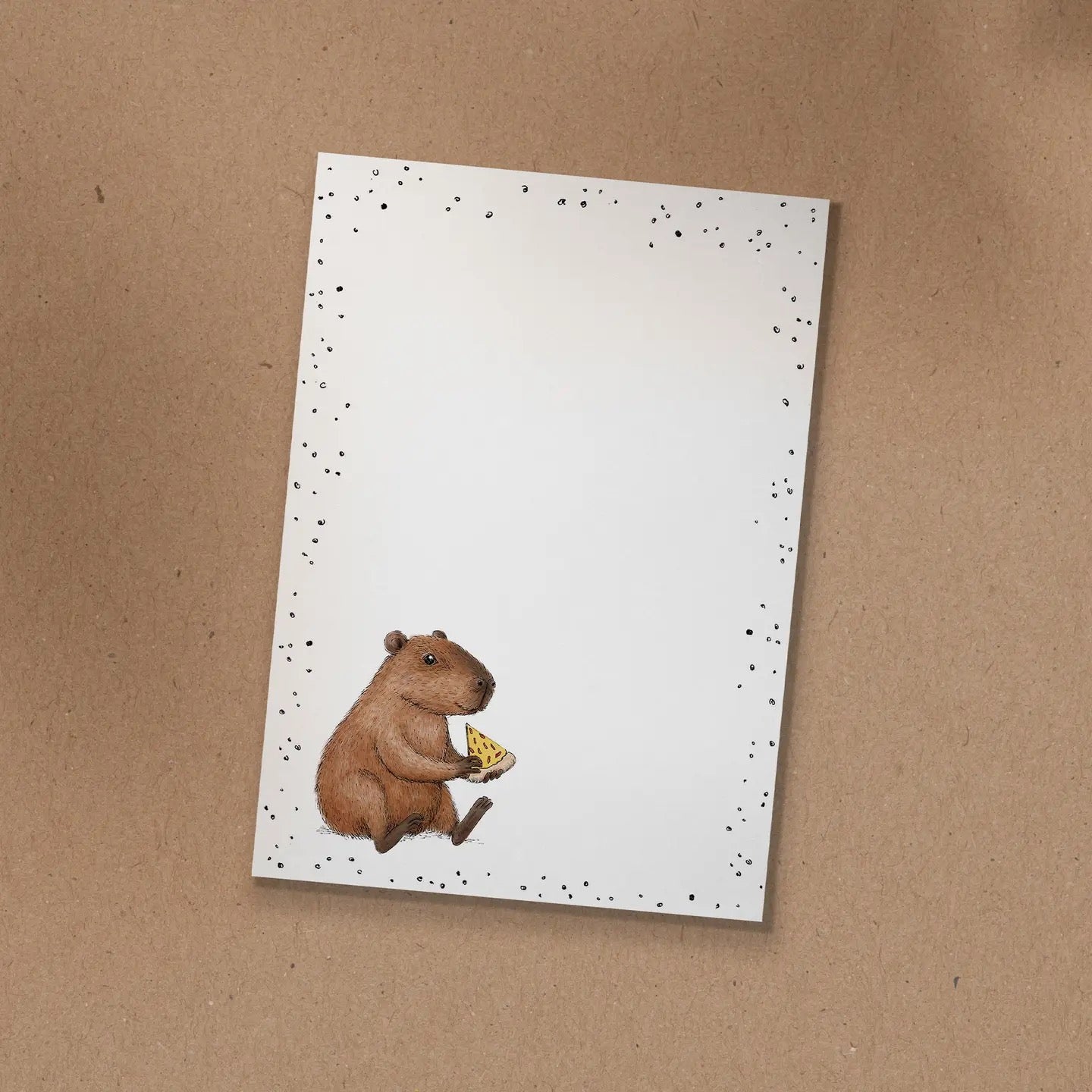 Notizblock mit handgezeichneter Illustration von Capybara Freddy, das ein Stück Pizza isst.