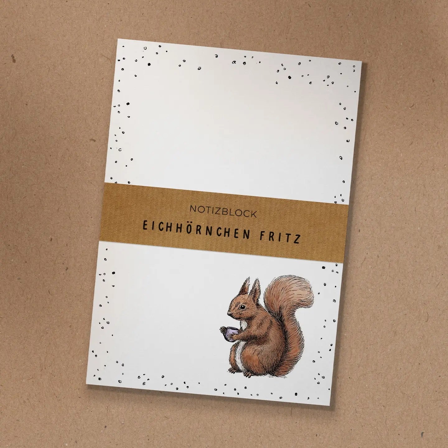 Notizblock mit Kraftpapier-Banderole und handgezeichneter Illustration von Eichhörnchen Fritz mit einer Kaffeetasse.