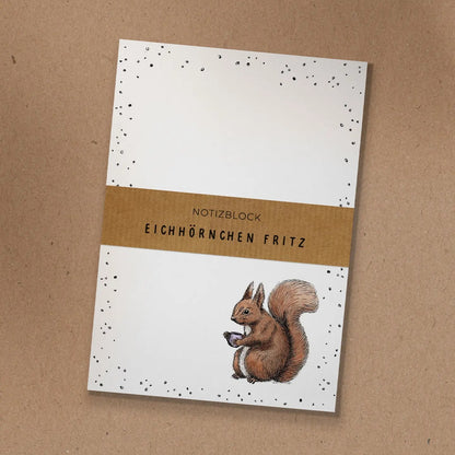 Notizblock mit Kraftpapier-Banderole und handgezeichneter Illustration von Eichhörnchen Fritz mit einer Kaffeetasse.