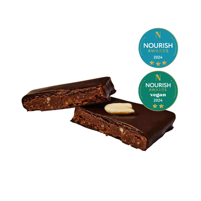 hier liegt ein halbierter Schokoladenriegel, der eine cremige Erdnussbutter-Füllung mit kleinen Nussstückchen offenbart. Die goldenen Siegel der „Nourish Awards 2024“ sind rechts oben platziert.