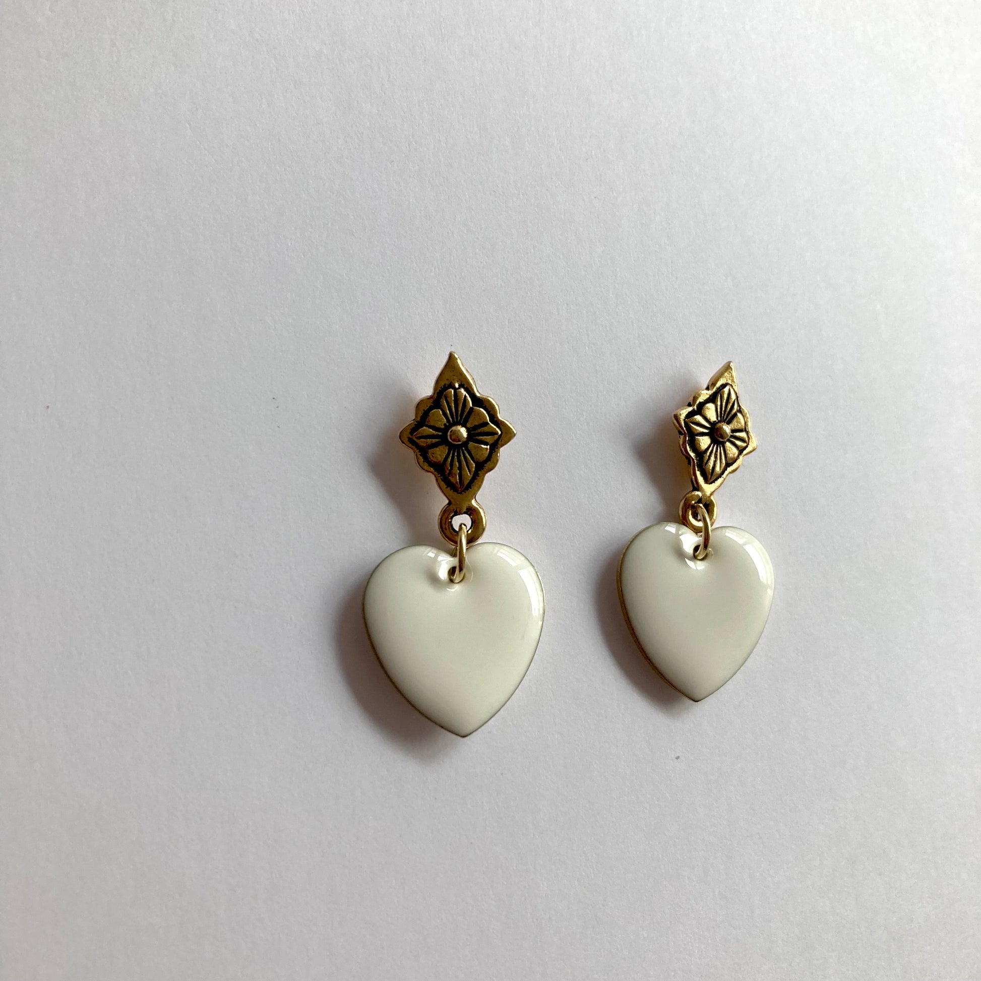 Ohrringe mit goldfarbenen, blumenförmigen Steckern und weißen, herzförmigen Anhängern.