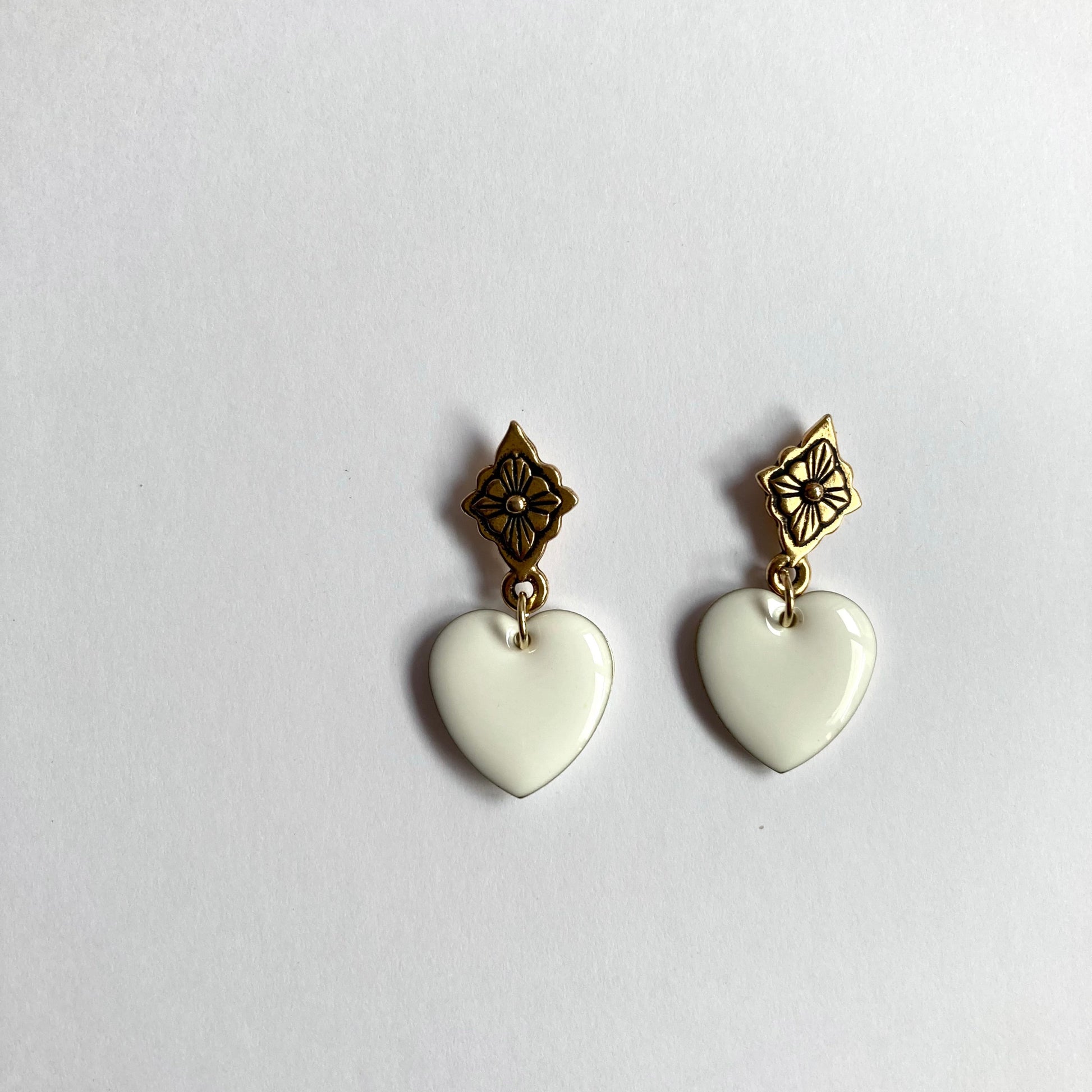 Ohrringe mit goldfarbenen, blumenförmigen Steckern und weißen, herzförmigen Anhängern.