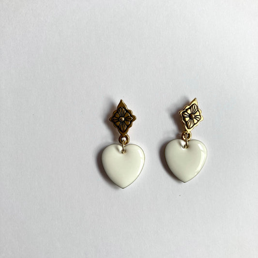 Ohrringe mit goldfarbenen, blumenförmigen Steckern und weißen, herzförmigen Anhängern.