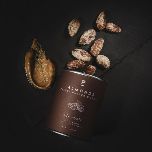 Dose mit Mandel-Peanut-Butter-Caramel-Aufschrift, daneben karamellisierte Mandeln und ein Klecks Erdnussbutter