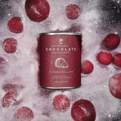 Beerenrote P-Stash Dose „Raspberry Chocolate Hazelnut“, umgeben von schwebenden rot-rosafarbenen Schoko-Haselnüssen und fein ausstäubendem weißem Puderzucker.