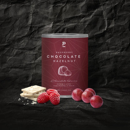 Dose mit Himbeer-Schokolade-Haselnuss-Geschmack, umgeben von weißen Schokoladenstücken, Himbeeren 