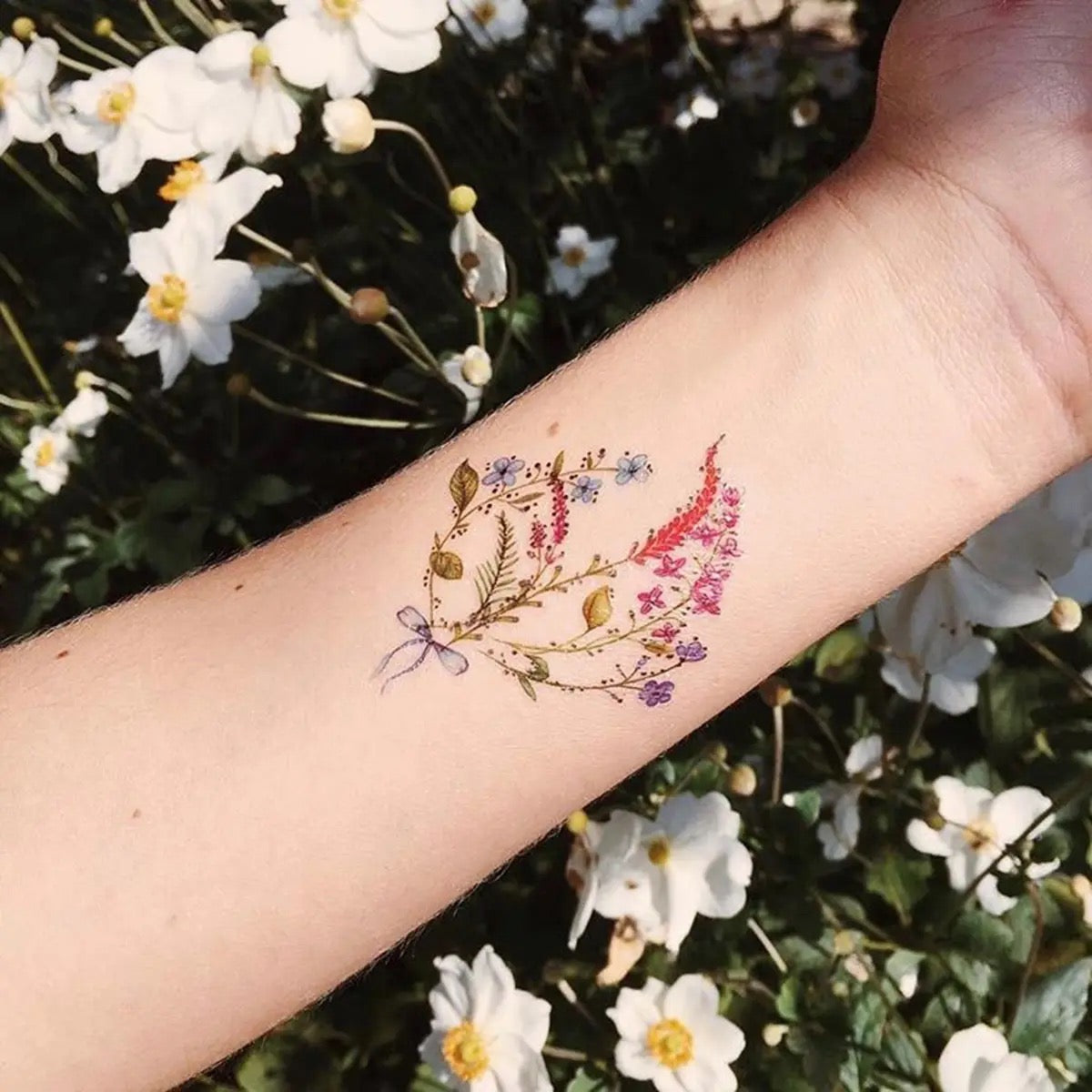 Unterarm mit feinem Tattoo aus verschiedenen kleinen Blumen und Blättern in zarten Farben