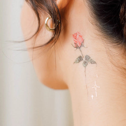 Hals einer Person mit einem kleinen, roten Rosen-Tattoo auf der rechten Seite und einem goldenen Ohrstecker