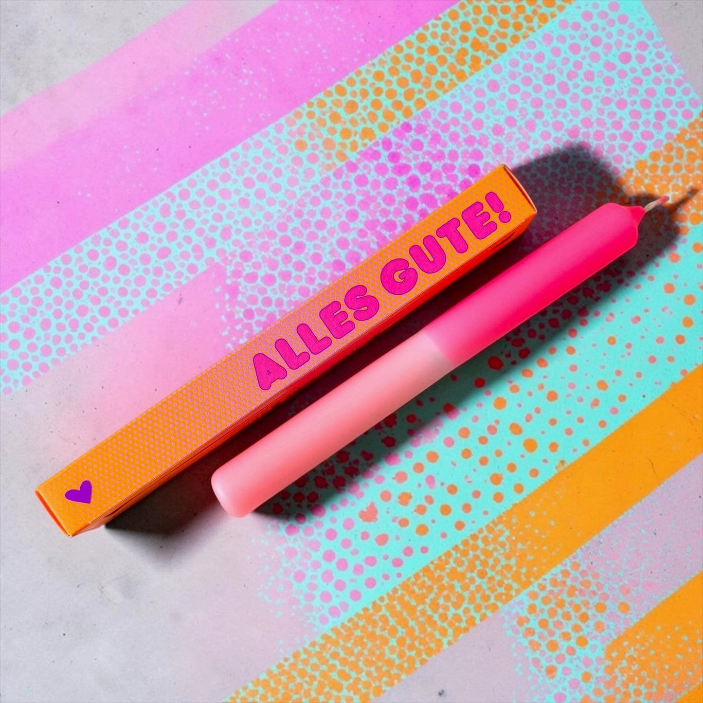 Pink Stories Dip-Dye Stabkerze in Neon Pink und Rosa mit ALLES GUTE! Verpackung auf buntem Hintergrund